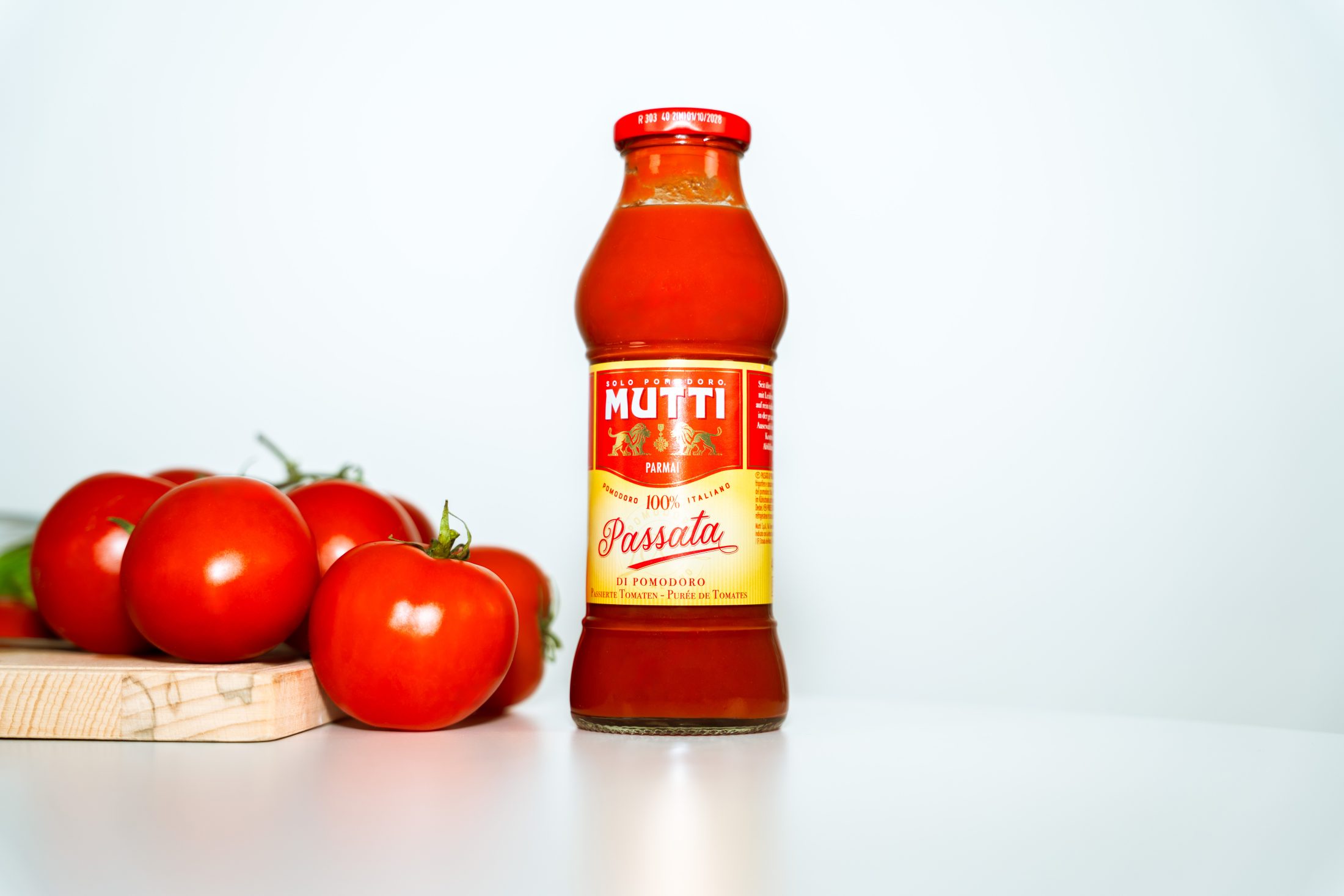 Minimalistisches Produkt Placement im Digital Marketing: Eine Flasche Mutti Passata Tomatensauce neben frischen Rispentomaten auf weißem Grund. SR-STUDIOS. | SR-STUDIOS