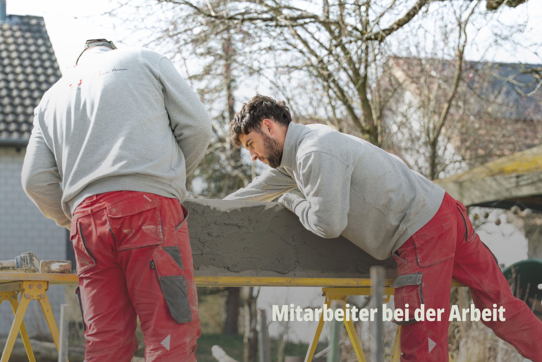 Handwerk im Fokus: Zwei Mitarbeiter der Vögtli Gartenbau GmbH arbeiten gemeinsam auf einer Baustelle an einer Terrassenplatte. Dynamisches Action Foto durch SR-STUDIOS, das Teamarbeit und Präzision vermittelt. | SR-STUDIOS