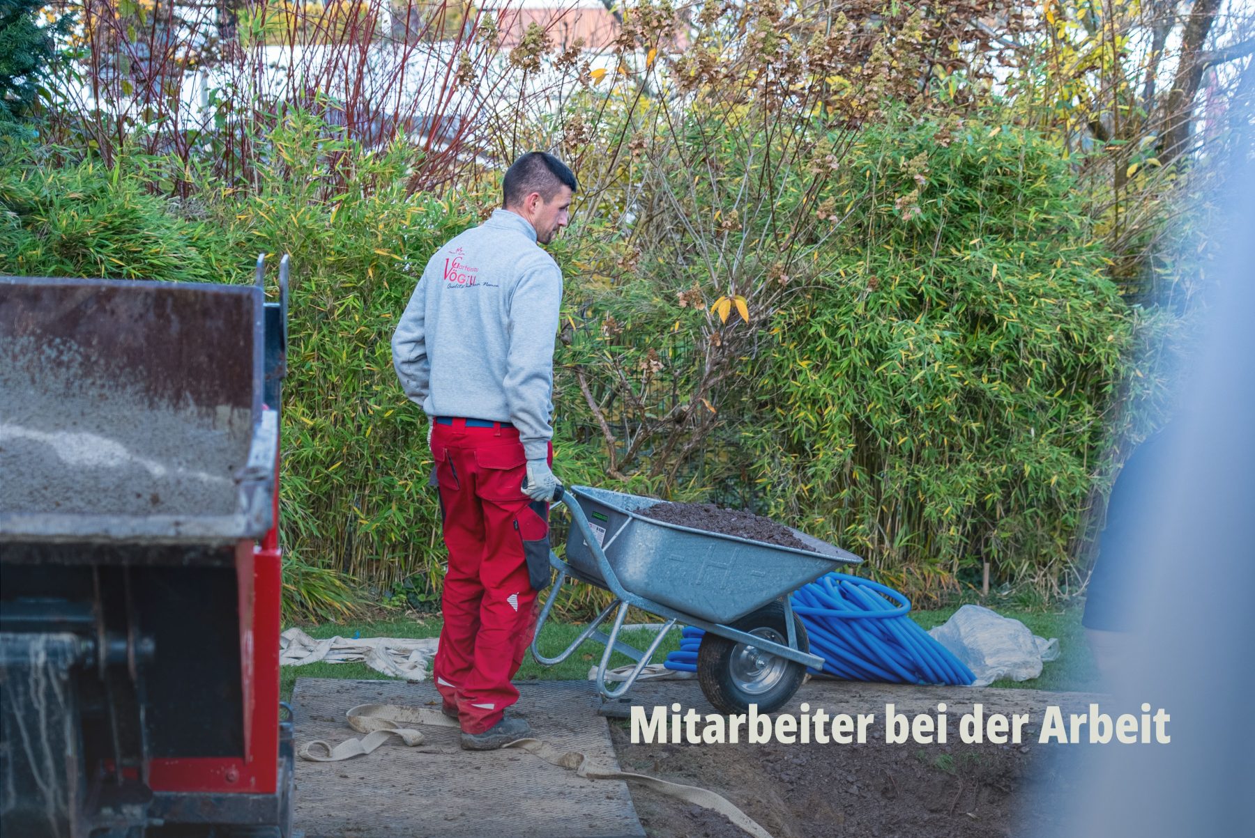 Werbefotografie im Gartenbau durch SR-STUDIOS: Ein Mitarbeiter von Vögtli Gartenbau in Arbeitskleidung schiebt eine voll beladene Schubkarre auf einer Baustelle. Fokus auf Bewegung und handwerkliche Aktivität. | SR-STUDIOS