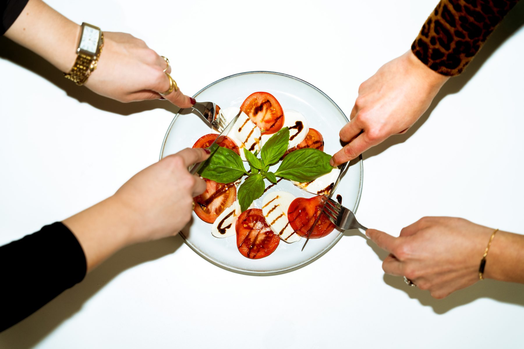 Social Media Marketing für Food Marken: Mehrere Hände greifen mit Gabeln nach einem frischen Caprese-Salat mit Tomaten auf einem Teller. SR-STUDIOS. | SR-STUDIOS