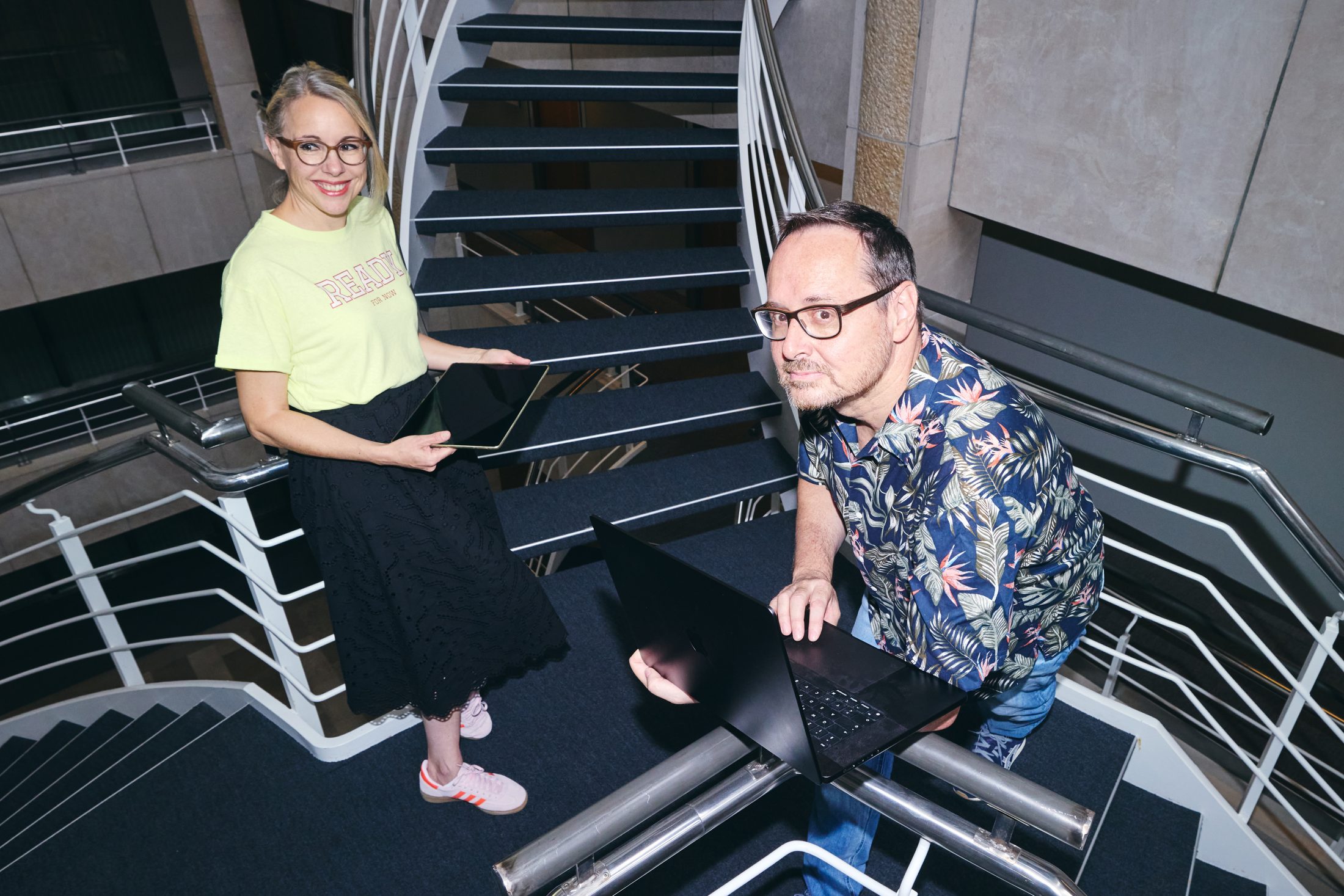 Agentur-Team stehend auf einer Treppe mit Laptop und Tablet. | SR-STUDIOS