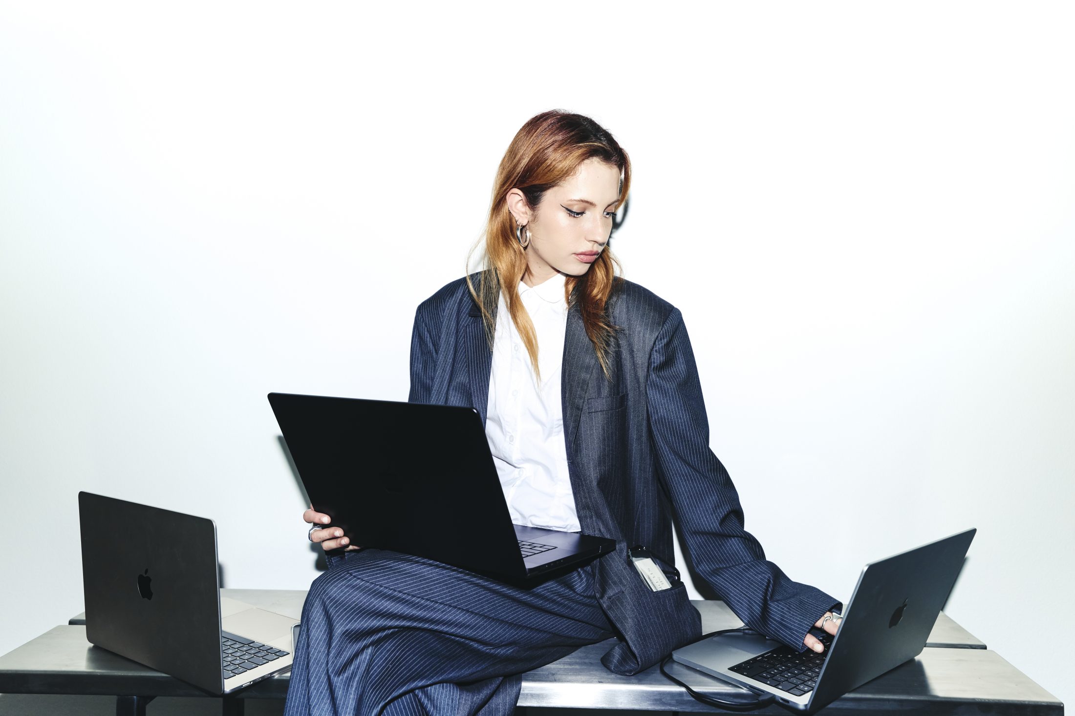 Junge Frau in stylischem Oversize Nadelstreifen Anzug sitzend auf einem Chrome-Schreibtisch mit Laptop. | SR-STUDIOS